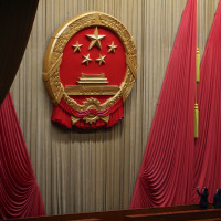 Workers adjust the curtain near the symbol of the National People's Congress (NPC) ahead of the closing session of the NPC at the Great Hall of the People in Beijing, Monday, March 11, 2024. 