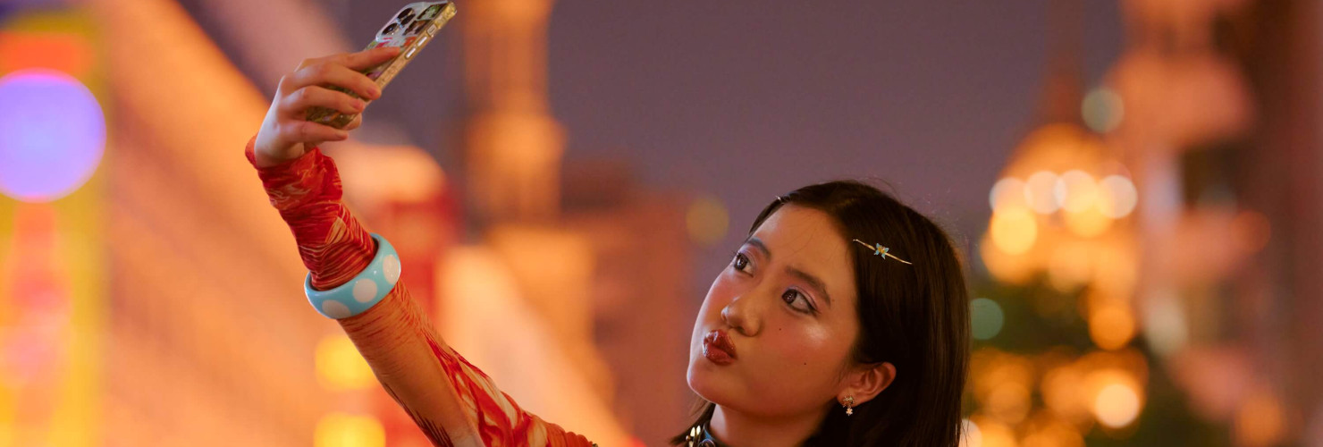 Young woman takes a selfie in vibrant, brightly lit city street in Shanghai, China, at night.