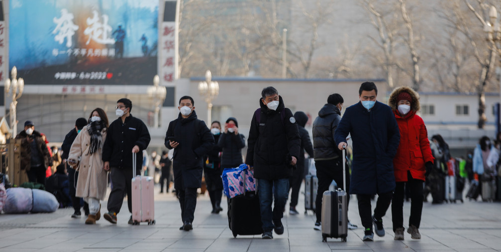 Passengers wearing face masks walk with their luggage in front of the Beijing Railway Station in Beijing, China, 10 January 2023.