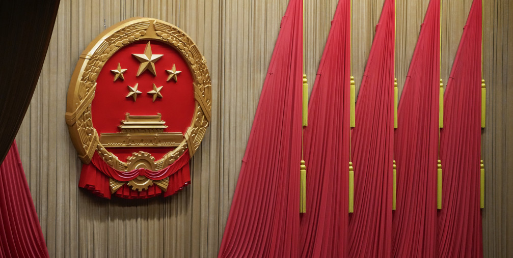 Workers adjust the curtain near the symbol of the National People's Congress (NPC) ahead of the closing session of the NPC at the Great Hall of the People in Beijing, Monday, March 11, 2024. 
