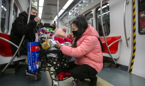 People wearing face masks attend to a child in a stroller as they ride a subway train in Beijing