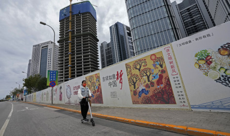 A girl wearing a face mask to help protect from the coronavirus rides a scooter past Chinese government's propaganda "China Dream" billboard on display along a commercial office buildings under construction in Tongzhou, outskirts of Beijing.