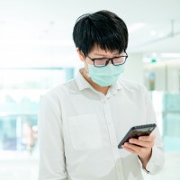 A man wearing a facemask looks at his smartphone