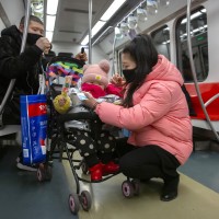 People wearing face masks attend to a child in a stroller as they ride a subway train in Beijing