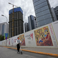 A girl wearing a face mask to help protect from the coronavirus rides a scooter past Chinese government's propaganda "China Dream" billboard on display along a commercial office buildings under construction in Tongzhou, outskirts of Beijing.