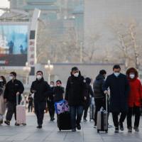 Passengers wearing face masks walk with their luggage in front of the Beijing Railway Station in Beijing, China, 10 January 2023.