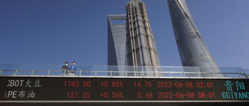 People stand on pedestrian bridge showing stock exchange data in Lujiazui