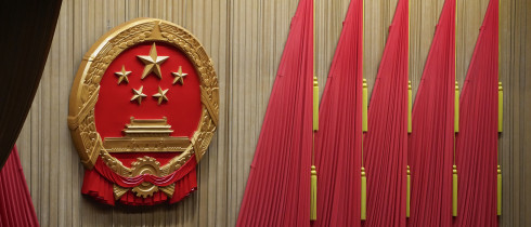 Workers adjust the curtain near the symbol of the National People's Congress (NPC) ahead of the closing session of the NPC at the Great Hall of the People in Beijing, Monday, March 11, 2024. 